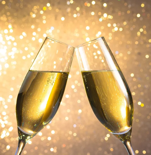 Par en champagne flöjter med gyllene bubblor på ljus bokeh bakgrund — Stockfoto