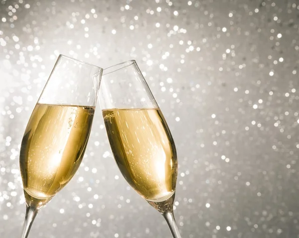 Champagne flutes with golden bubbles on silver light bokeh background — Stock Photo, Image