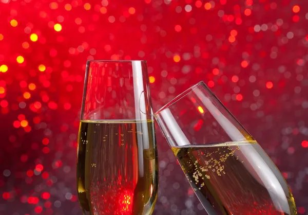 Two champagne flutes with gold bubbles on red light bokeh background — Stock Photo, Image