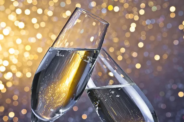 Champagne flutes with golden bubbles on light bokeh background — Stock Photo, Image