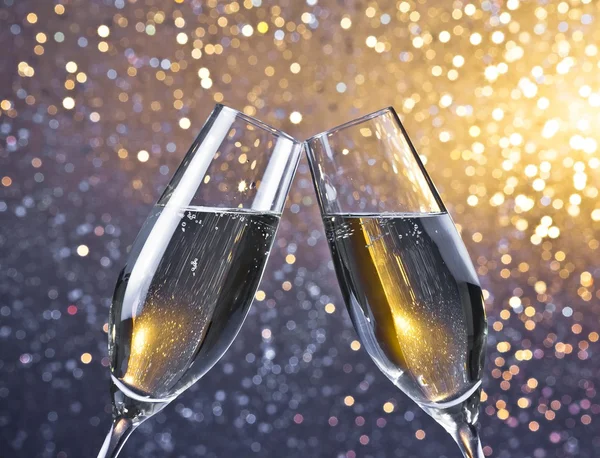 Cheers met twee champagne fluiten met gouden bubbels op lichte bokeh achtergrond — Stockfoto