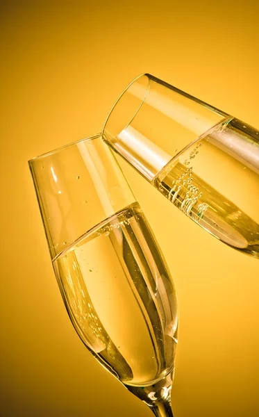 Two champagne flutes with golden bubbles on golden light background — Stock Photo, Image