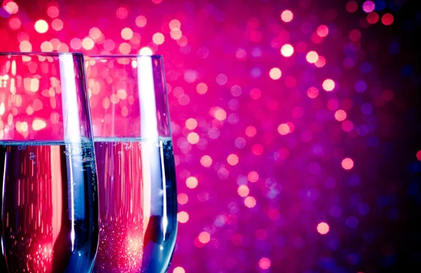 Champagne flutes with gold bubbles on blue and violet tint light bokeh background — Stock Photo, Image