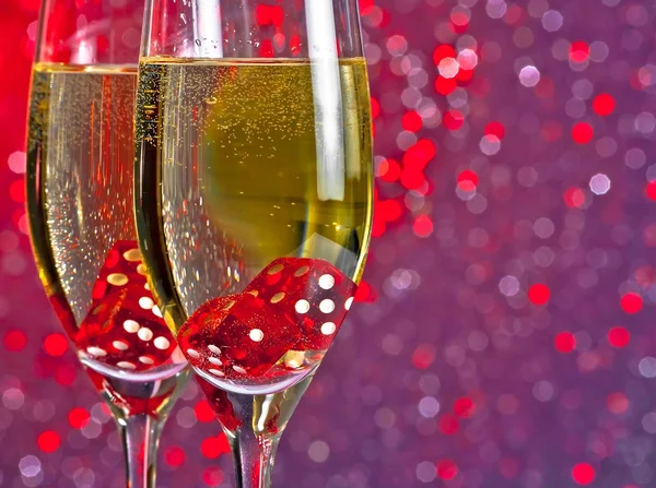 Červené kostky klesá v šampaňské flétny na odstín červené a fialové světlo bokeh pozadí — Stock fotografie