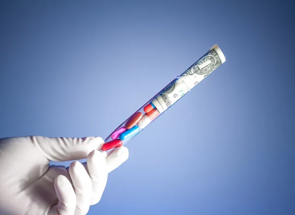 Colorful pills and dollars in test tube in a hand, cost of medical health care — Stock Photo, Image