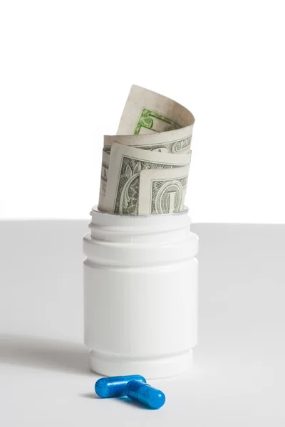 Detail of blue pills in front of container with inside rolled up dollars on white background — Stock Photo, Image