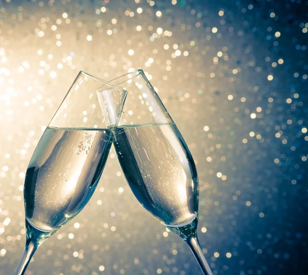 Champagne flutes with golden bubbles on blue light bokeh background — Stock Photo, Image