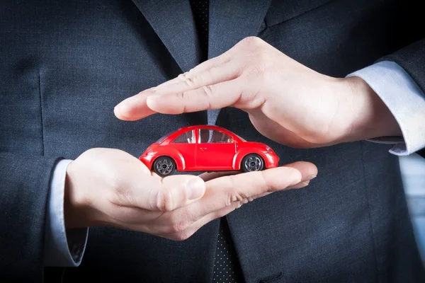 Geschäftsmann schützt mit seinen Händen ein rotes Auto, Versicherungs-, Kauf-, Miet-, Kraftstoff- oder Service- und Reparaturkosten Stockfoto