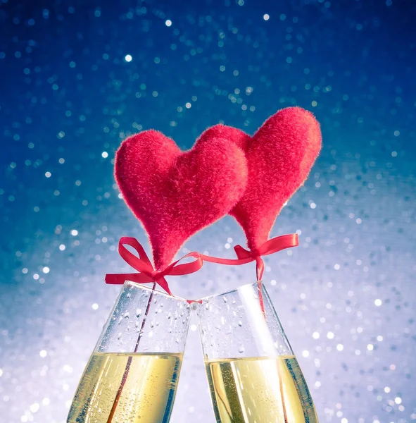 Champagne flutes with golden bubbles and red velvet hearts make cheers on blue bokeh background — Stock Photo, Image