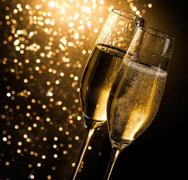 Champagne flutes with golden bubbles on dark golden light bokeh background — Stock Photo, Image