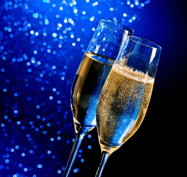 Champagne flutes with golden bubbles on dark blue light bokeh background — Stock Photo, Image