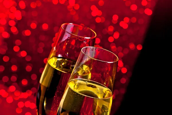 Champagne flutes with golden bubbles on dark red light bokeh background — Stock Photo, Image