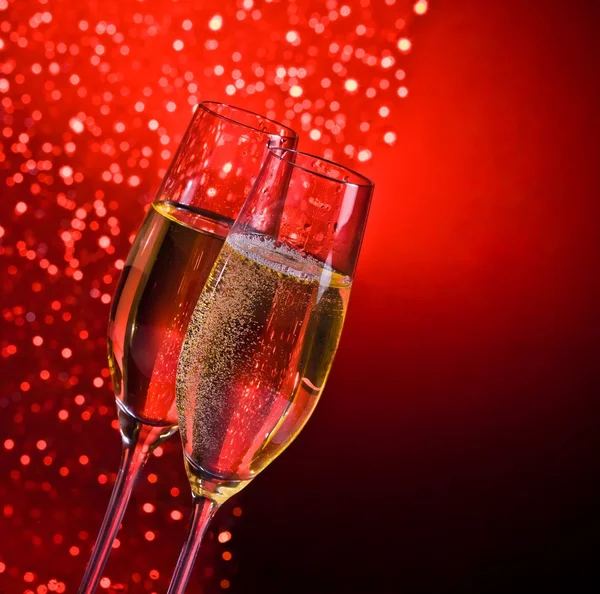 Champagne flutes with golden bubbles on dark red light bokeh background — Stock Photo, Image