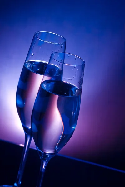 Taças de champanhe na mesa de bar no fundo de luz azul escuro e violeta — Fotografia de Stock