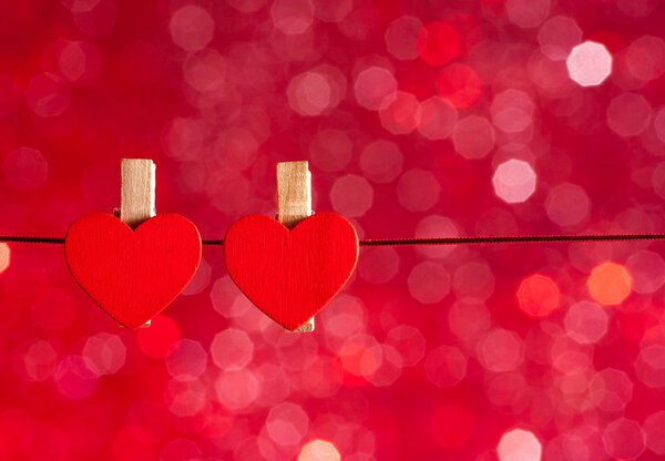 two decorative red hearts hanging against red light bokeh background, concept of valentine day