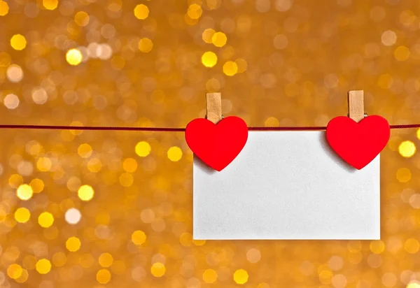 Deux cœurs rouges décoratifs avec carte de vœux suspendue sur fond bokeh lumière dorée, concept de Saint Valentin — Photo