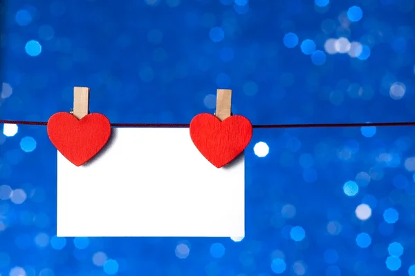 Deux cœurs rouges décoratifs avec carte de vœux suspendue sur fond bleu clair bokeh, concept de Saint Valentin — Photo