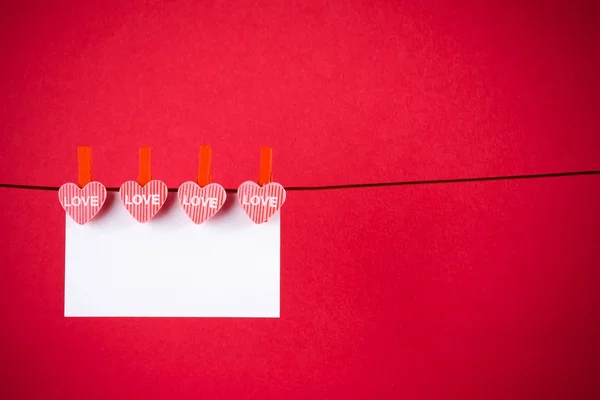 Corazones rojos decorativos con tarjeta de felicitación colgando en el fondo rojo, concepto de día de San Valentín —  Fotos de Stock