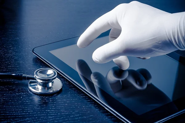 Mano en el guante médico tocando la tableta digital moderna PC cerca del estetoscopio —  Fotos de Stock