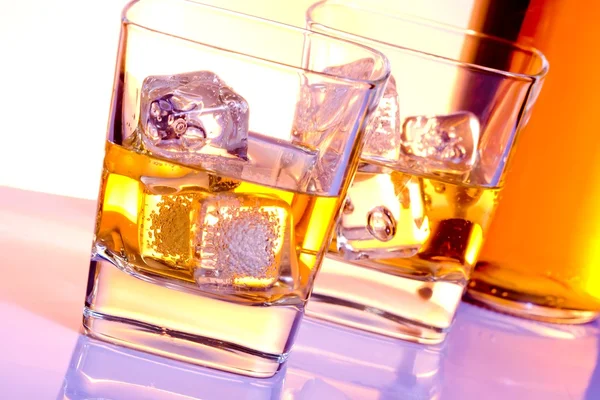 A pair of glasses of whiskey with ice on disco violet light — Stock Photo, Image