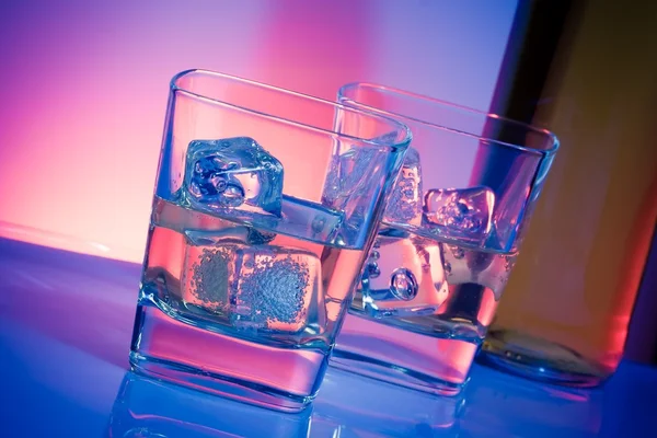 A pair of glasses of drink with ice on disco violet light — Stock Photo, Image
