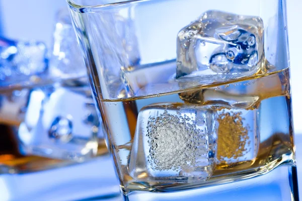 A pair of glasses of alcoholic drink with ice on disco blue light — Stock Photo, Image