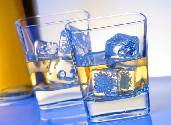 Two glasses of whiskey with ice on blue light — Stock Photo, Image
