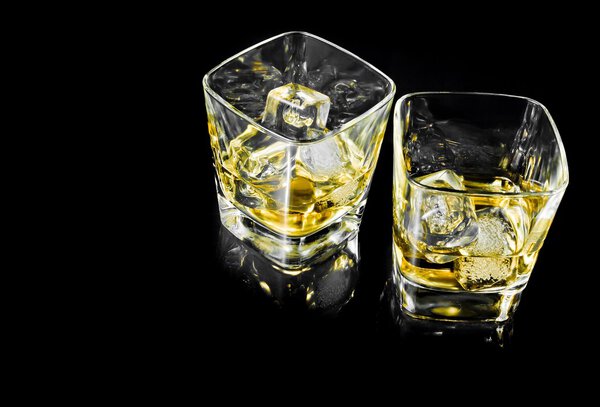 two glasses of alcoholic drink with ice on black background