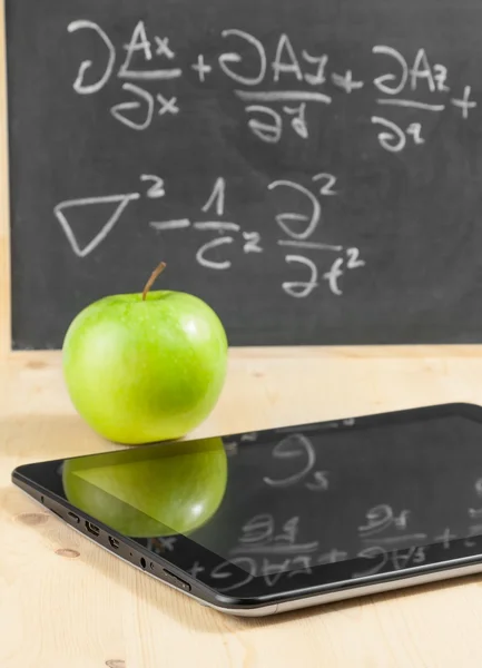 tablet pc and green apple in front of blackboard on wood table