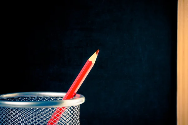 Red pencil in container against empty blackboard — Stock Photo, Image