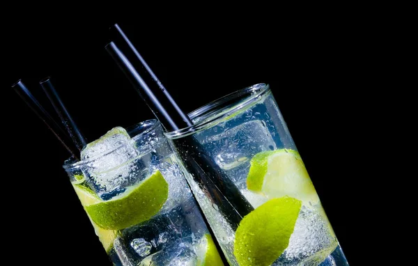 Due bicchieri con cocktail e ghiaccio con fetta di lime su fondo nero con spazio per il testo — Foto Stock