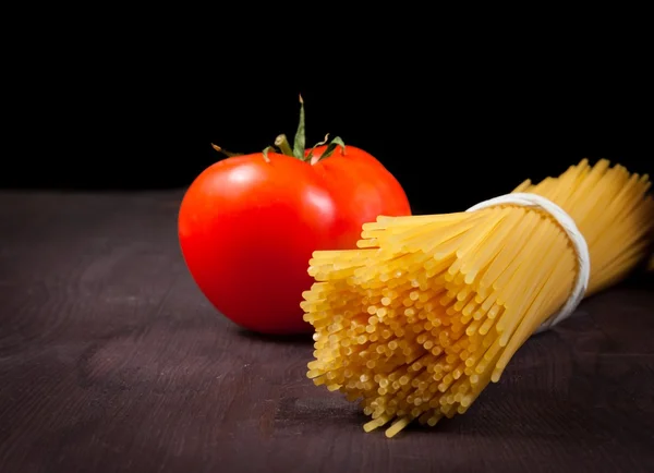 Manojo de espaguetis de pasta cruda con tomate sobre mesa de madera —  Fotos de Stock