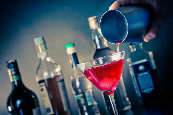 Barman derramando um coquetel vermelho em um copo com gelo — Fotografia de Stock