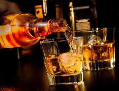 Barmen önünde viski bardak ve şişe viski yağıyor