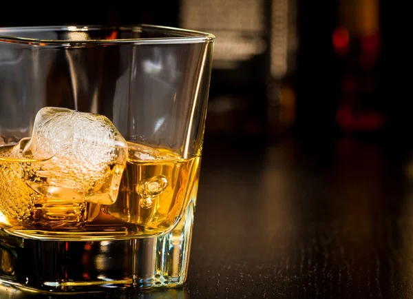 Whiskey glass with ice in front of bottles with space for text — Stock Photo, Image