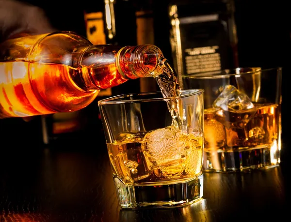 Barmann gießt Whisky vor Whiskeyglas und -flasche Stockfoto