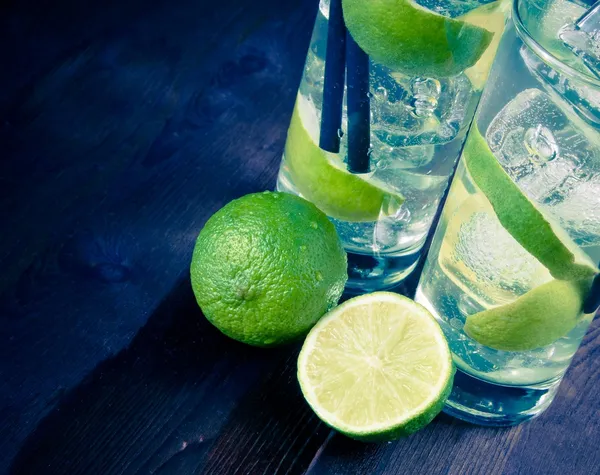 Dettaglio di due bicchieri con cocktail e ghiaccio con fetta di lime su fondo legno antico — Foto Stock