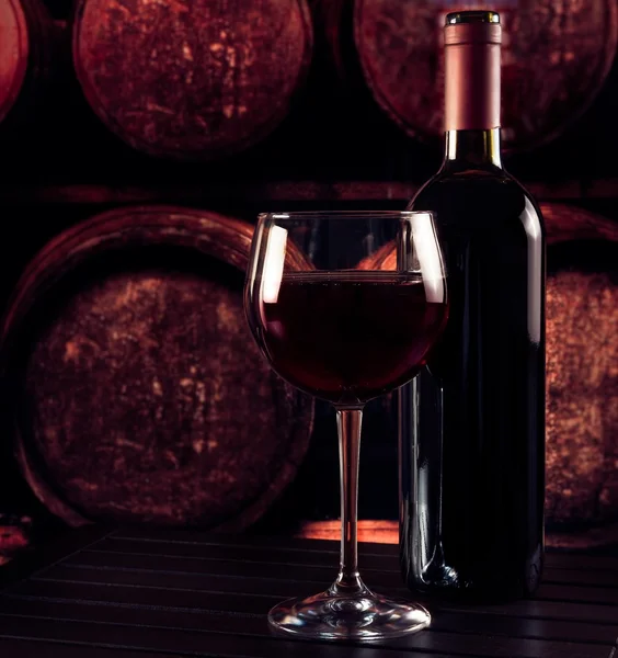 Red wine glass near bottle on wood table and in old wine cellar background — Stock Photo, Image