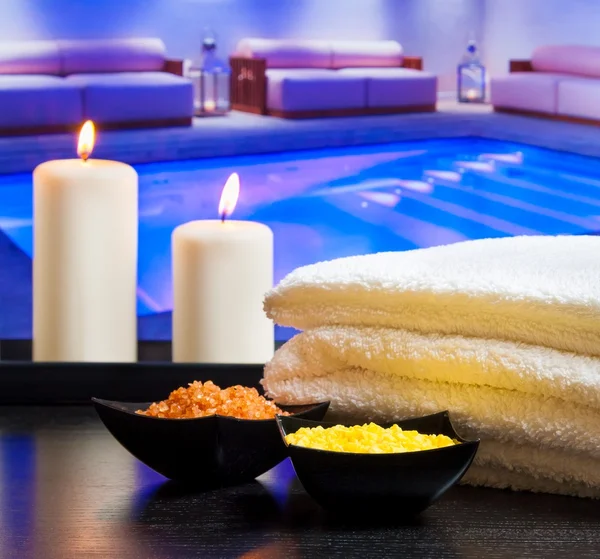 Spa massagem borda fundo com toalha velas empilhadas e sal marinho perto da piscina — Fotografia de Stock