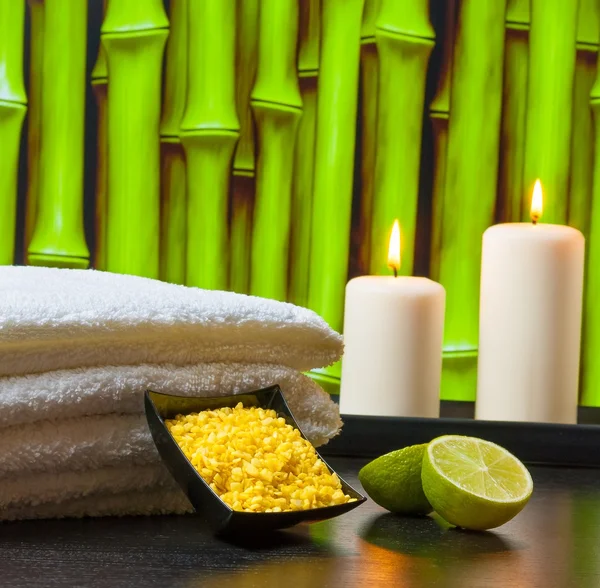 Spa massagem borda fundo com toalha empilhadas velas de sal do mar e limão — Fotografia de Stock