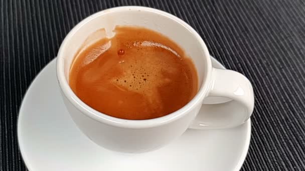 커피 한 컵 안에 들어가는 커피는 매우 느린 속도로 흘러가고 있습니다. 커피 안 에는 검은 색 배경 위에 거품 이 있고 음식 과 음료가 담겨 있습니다. — 비디오