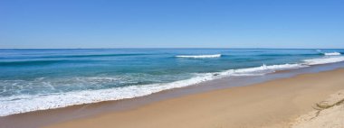 A peaceful scene of surf waves rolling onto a sandy beach along the shore at Kawana on the Sunshine Coast Queensland Australia on a sunny winter day.