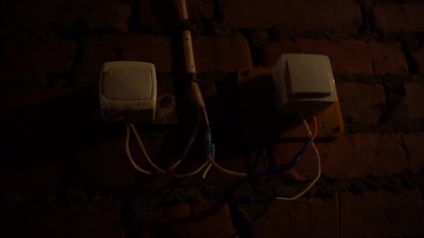Stare białe przełączniki na ceglanej ścianie w ciemnej piwnicy, przewody owinięte taśmą izolacyjną powodującą pożar — Wideo stockowe