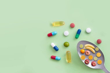 Elma, muz, kireç ve portakalların yanı sıra vitamin hapları ve kapsüller içeren kaşık.