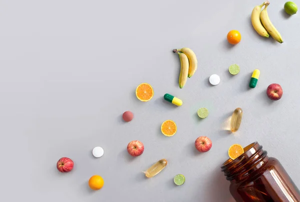 维生素丸和胶囊 以及从药罐中取出的苹果 石灰和橙子 营养概念 图库图片