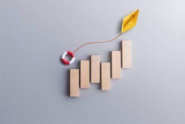Finansal başarı kurtarma konsepti, kağıt tekneyle tahta bloklar, yukarı doğru hareket eden bir can simidi taşıyan bir şamandıra. 