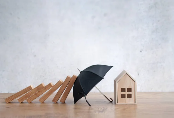 Umbrella protecting house from falling dominoes, insurance concept
