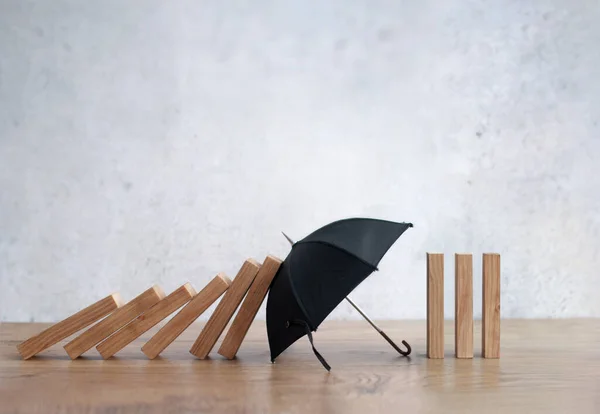 Umbrella protecting wooden dominoes insurance concept