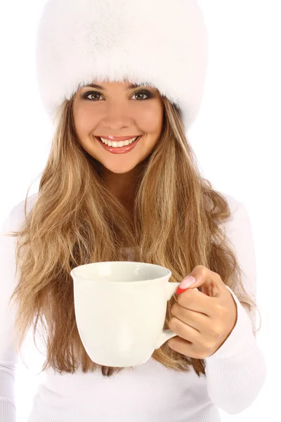 Attractive girl in white fur hat gives white mug — Stock Photo, Image