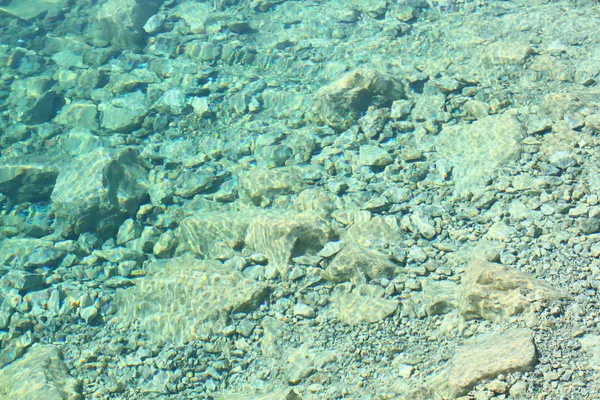 Sea water with sunlight on turquoise pebbles background — Stock Photo, Image